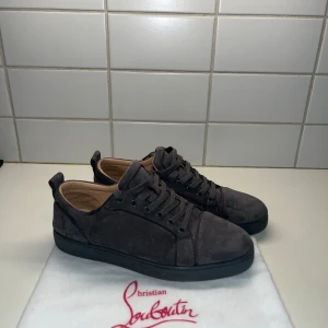 Grå sneakers från Christian Louboutin - Snygga grå sneakers i mocka från Christian Louboutin med den ikoniska röda sulan. Skorna har snörning och en stilren design som passar perfekt för en trendig look. Insidan av vänstra skon har ett litet slitage (se sista bilden) men det är inget man märker. Tveka inte på frågor och prisförslag💯🔥