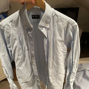 Ljusblå skjorta från Tiger of Sweden - Snygg ljusblå skjorta från Tiger of Sweden i slim fit. Skjortan har långa ärmar och klassiska knappar framtill. Perfekt för en stilren look.