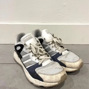 Adidas sneakers  - Snygga Adidas sneakers med Cloudfoam-sula för extra komfort. Skorna har en vit och grå färgkombination med svarta och orange detaljer. De har klassisk snörning och en robust yttersula. Perfekta för en avslappnad stil.