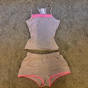 Grå pyjamas set med rosa spets från H&M  - Säljer det här supergulliga toppen från H&M med smala axelband och fina rosa spetsdetaljer vid bysten. Matchande shorts med rosa spetskant ingår.Storleken är barn 146-152 men passar även som XS. Använd fåtal gånger därav mycket bra skick. 