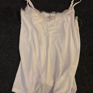 Vit linnetopp från Amisu - Säljer en elegant vit linnetopp från Amisu med spetsdetaljer vid halsringningen. Knappt använd 