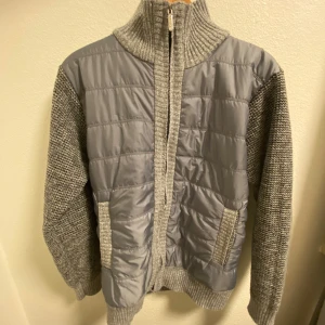 Grå cardigan jacka - Säljer en snygg grå cardigan jacka med quiltade detaljer på framsidan. Jackan har en hög ribbad krage och långa ärmar. Perfekt för kyliga dagar!