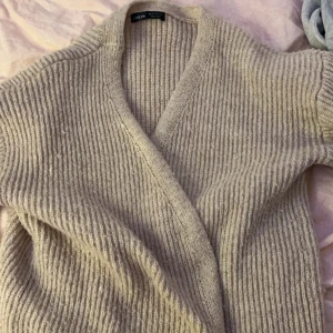 Beige stickad kofta från Shein - Mysig beige stickad kofta från Shein med ribbad struktur. Perfekt för kyliga dagar med sin mjuka och bekväma passform. Koftan har en enkel design som gör den lätt att matcha med olika outfits.