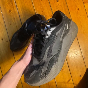 Svarta Puma sneakers - Säljer ett par svarta sneakers i bra skick. De har en cool design med olika texturer och mönster på ovansidan. Skorna har snörning och en robust sula som ger bra grepp. Perfekta för vardagsbruk eller träning!