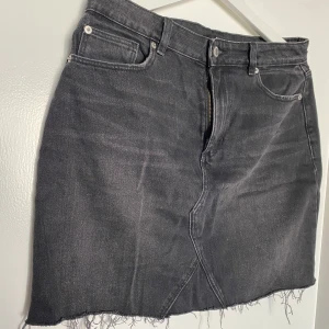 Jeans kjol - Svart/grå jeans kjol från bikbok, strl 40. Har slitningar och fickor både bak- och framtill. Använd ett fåtal gånger. Fin passform som går in i midjan. Silverdetaljer. Priset är alltid diskuterbart🌸