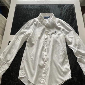 Mycket stilig Polo Ralph Lauren skjorta - Vit färg, Slim fit modell, Storlek M    Tyvärr så har skjortan en pytteliten fläck vid slutet av baksidan, fläcken borde dock ej synas i överhuvudtaget ifall om man lägger in skjortan in i byxan!