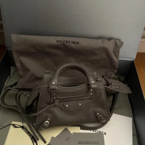 Balenciaga neo mini väska - Fin Balenciaga neo mini Classic bag. Använd fåtal gånger. Färgen är grå, med silvriga detaljer.   Mått ca: L20cm x H15cm x D7cm  Material: Grained kalvskinn. Nypris var runt 17 000kr.   Box, dustbag och tags medkommer vid köp.