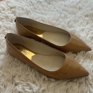 Beige ballerinaskor från Michael Kors - Beige ballerinaskor från Michael Kors med glansig finish och spetsig tå, med en elegant look. Gjorda av skinn. Perfekt till vardag och fest. Använda 1 gång då dom är för små. Storlek 36/36,5 men passar perfekt för dig som bär storlek 37!🌺