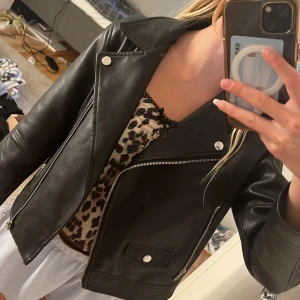 Svart skinnjacka från Zara - Säljer en snygg svart skinnjacka från Zara. Den har en klassisk bikerstil med dragkedja och knappar. Perfekt för att ge din outfit en cool edge. Jackan är i bra skick och redo för nya äventyr!