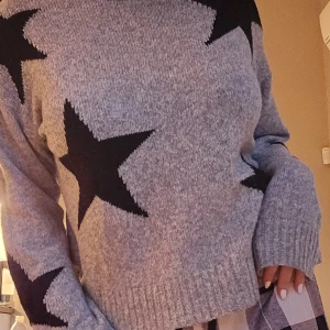 Grå stickad tröja - Denna tröjan är stickad och passar perfekt till kallare klimat som höst och vinter. Tröjan är grå med svarta stjärnor där fram. Den är inte överdrivet oversize vilket jag tycker är väldigt fint i sig. 