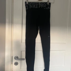 Svarta Nike Pro leggings - Säljer ett par svarta Nike Pro leggings i storlek M. De är tillverkade i Dri-FIT-material som håller dig torr och bekväm under träning. Högmidjade med en bred resår i midjan för extra stöd. Perfekta för gymmet eller löprundan!