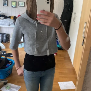 Grå croppad hoodie - Säljer en superfin grå croppad hoodie med trekvartsärmar. Den är perfekt för en avslappnad stil och har en mysig huva med snören. Passar perfekt till jeans eller leggings för en chill look. Perfekt för vår och sommar!