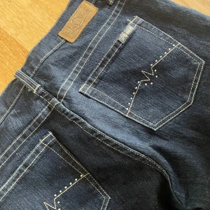 Snygga Jeans - Säljer ett par mörkblå jeans från Saddler i storlek 30. De har snygga broderade detaljer på bakfickorna och en klassisk femficksdesign. Jeansen är i bra skick och passar perfekt för både vardag och fest. Materialet är en blandning av bomull och polyester för extra komfort. 💖