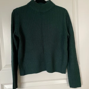 Mörkgrön ribbad tröja från H&M Divided - Säljer en snygg mörkgrön ribbad tröja från H&M Divided. Perfekt för höst och vinter med sin mysiga och varma känsla. Tröjan har långa ärmar och en hög krage som håller dig varm. Passar perfekt till både jeans och kjol!