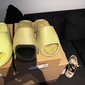 Säljer ett par Adidas Yeezy Slide i en snygg beige färg. De är i bra skick och perfekta för sommaren. Slidesen har en modern och minimalistisk design med öppen tå och är superbekväma att ha på sig. Perfekta för både stranden och hemma. Kommer i originalförpackning.