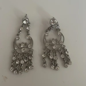 Glittriga silverörhängen med hängande detaljer - Säljer ett par superfina glittriga örhängen i silver. De har en elegant design med hängande kedjor och gnistrande stenar som fångar ljuset perfekt. Perfekta för fest eller en utekväll när du vill glänsa lite extra! ✨