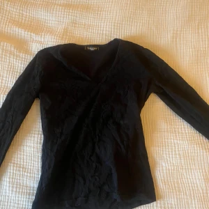 Svart långärmad topp från Sinequanone - Snygg svart topp från Sinequanone med v-ringning och diskret mönster. Perfekt för både vardag och fest. Den är långärmad och har en elegant passform som funkar året runt. Ett måste i garderoben för en stilren look!