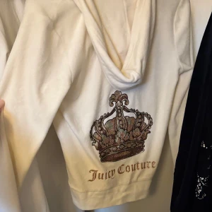 Vit hoodie från Juicy Couture - Säljer en superfin vit hoodie från Juicy Couture i storlek M. Den har en glittrig krona och logga på ryggen, vilket ger den en lyxig touch. Perfekt för en chill dag eller en avslappnad fest. Dragkedja framtill och långa ärmar gör den både praktisk och snygg.