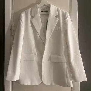 Vit kavaj från Gina Tricot - Säljer en vit kavaj från Gina Tricot i storlek XS. Perfekt för både vardag och fest med sin klassiska design och långa ärmar. Kavajen har en snygg passform och är tillverkad i ett bekvämt material. Den är lite oversized