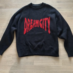 Svart oversize tröja Weekday med röd text - Säljer en cool svart tröja med röd text 'DREAM CITY' på framsidan. Tröjan har en avslappnad passform och är perfekt för höst och vinter. Den är långärmad och gjord i ett mjukt material som håller dig varm. Perfekt för en casual look.