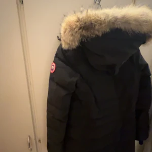 Svart dunjacka med päls från Canada Goose - Säljer en svart dunjacka från Canada Goose som är äkta i mycket bra skick. Jackan har en stor, fluffig päls på huvan och är perfekt för kalla vinterdagar