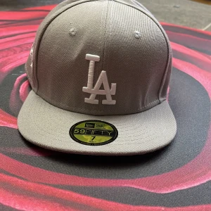 Grå keps från New Era - Helt ny grå keps från New Era med LA-logga. Den har en broderad World Series-logga på sidan och MLB-logga bak. Kepsen är i nytt skick och har en klassisk passform. Har storlek 7/55,8 cm
