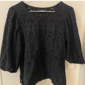 Svart blus från KappAhl - Snygg svart blus från KappAhl med trekvartsärm och ett vackert broderat mönster. Perfekt för både vardag och fest! Blusen är liten i storleken och passar s/m. Passar bra till jeans eller kjol för en stilren look.