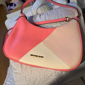 Flerfärgad axelväska från Michael Kors - Säljer en superfin axelväska från Michael Kors i rosa, ljusrosa och vit. Väskan är i skinn och har en elegant design med guldfärgad logga framtill. Perfekt för både vardag och fest! 👜✨Endast använd 2 gånger.