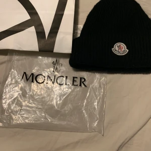 Svart moncler mössa - Säljer min moncler mössa för att jag vill inte ha den längre, 9/10skick inget täcken på användning. Har tyvärr inget kvitto pågrund av att jag slängde det när lämna tillbaks datumet gick ut. jag är öppen för byten