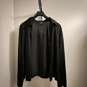 Svart skjorta - Snygg svart skjorta från add it i storlek 42/44. Den har långa ärmar och knappar framtill. Oanvänd!