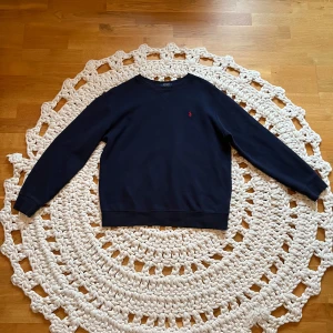 Mörkblå tröja från Polo Ralph Lauren - Säljer en snygg mörkblå tröja från Polo Ralph Lauren med det klassiska röda broderade logotypen på bröstet. Tröjan är i mycket bra skick och perfekt för både höst och vår. Den har långa ärmar och är gjord i ett mjukt bomullsmaterial. Den är i storleken 170 (S) Med en liten defekt på men går lätt bort i tvätt