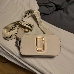 Beige axelväska från Marc Jacobs, the snapshot - Säljer en superfin beige axelväska från Marc Jacobs. Den har en justerbar axelrem med loggan tryckt i svart. Väskan har två dragkedjor och en snygg metallogo på framsidan. Perfekt för både vardag och fest! 👜✨Använd endast en gång 