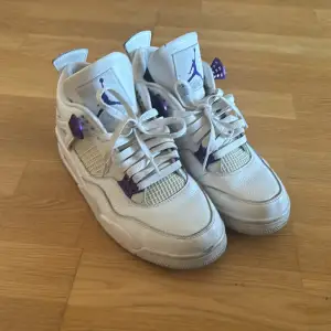 Säljer ett par snygga Nike Air Jordans i vitt med lila detaljer. Skorna har klassisk snörning och är i bra skick. Perfekta för både vardag och fest! De har en cool design med den ikoniska Jumpman-loggan på tungan och hälen.