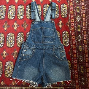 Jeansshorts med hängslen - Säljer ett par coola jeansshorts med hängslen i klassisk blå denim. Köpta från Brandy Melville och har aldrig användts!