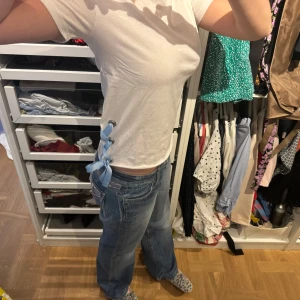 Vit t-shirt med blå snörning - Säljer en vit t-shirt i bomull med en unik blå snörning på sidan. Den har en normal passform och korta ärmar, perfekt för sommaren!