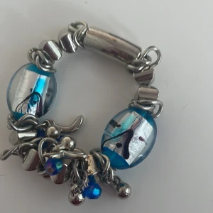 Blått och silverfärgat armband med pärlor - Snyggt armband med stora blå och silverfärgade pärlor. Armbandet har också små blå glittriga detaljer och silverfärgade metallpärlor. Perfekt för att ge en färgklick till din outfit! Passar både till vardags och festliga tillfällen. Ny