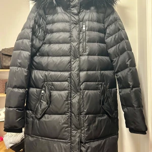 Svart dunjacka med pälshuva - Säljer en svart lång dunjacka från Vero Moda mycket bra skick använd endast 1 gång. Den har en mysig pälshuva som går att ta av med dragkedja och tryckknappar på fickorna.  Perfekt för kalla vinterdagar! Jackan är långärmad och har ribbade muddar för extra värme. Passar både till vardags och festliga tillfällen. Skickas med spårbar frakt men går även att hämta i Malmö. Storlek M men passar även en S. Nypris 1199:- 