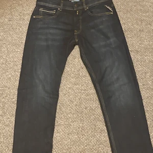 Mörkblå jeans från Replay - Säljer ett par snygga mörkblå jeans från Replay i mycket bra skick. De har en klassisk femficksdesign med gul kontrastsöm och en läderpatch med Replay-logga på baksidan. Perfekta för både vardag och fest!