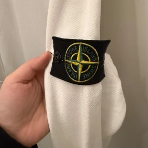 Vit tröja från Stone Island - Säljer en stilren vit tröja från Stone Island. Den har en klassisk design med långärmade ärmar och en rund halsringning. Tröjan är i mycket bra skick och har det ikoniska Stone Island-märket på ärmen. Perfekt för både vardag och fest!