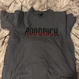 Grå t-shirt från Hoodrich - Säljer en grå t-shirt från Hoodrich i storlek S. Den har en cool logga i svart och rött på framsidan. Perfekt för en avslappnad stil och passar till alla tillfällen. T-shirten är i bra skick och gjord av mjukt material.