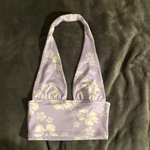 Lila blommig Top - Säljer en superfin lila Top med blommigt mönster i vitt. Den har en halterneck-design som knyts runt nacken och ger en bekväm passform. Perfekt för sommarens stranddagar eller poolhäng! 🌸