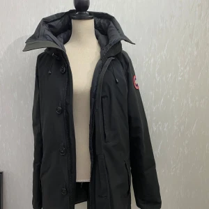 Svart Canada Goose - Svart parkajacka från Canada Goose i mycket bra skick. Den har både dragkedja och knappar för extra skydd mot kyla. Supervarm och stilren!