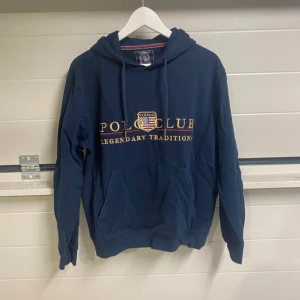 Mörkblå hoodie från Polo Club - Säljer en snygg mörkblå hoodie från Polo Club med texten 'Legendary Traditions' på framsidan. Den har en klassisk känguruficka och en bekväm huva. Perfekt för en avslappnad stil eller kyliga dagar. Passar både till vardags och chillkvällar.