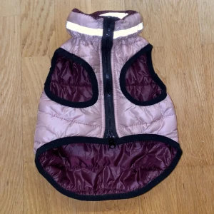 Lila quiltad hundjacka - superfin lila quiltad hundjacka i storlek 45 cm. Den är gjord av 100% polyester och har en praktisk dragkedja framtill. Perfekt för kyliga höst- och vinterpromenader. Jackan har en reflekterande rand på kragen för extra säkerhet i mörkret. 🐾använd av min hund som valp endast 2-3 gånger