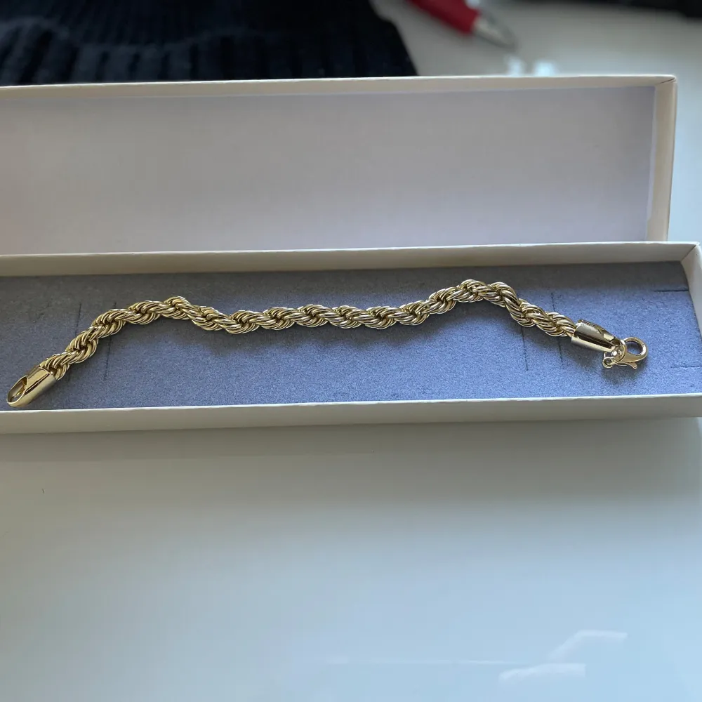 Säljer ett elegant guldarmband med en tvinnad design. Armbandet har en fin glans och kommer i en snygg presentask. Perfekt för att ge bort som present eller för att lyxa till din egen smyckessamling. Låset är enkelt att använda och håller armbandet säkert på plats.. Accessoarer.