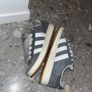 Säljer ett par gråa Adidas sneakers i bra skick. De har klassiska vita ränder på sidan och en snygg retrostil. Perfekta för vardagsbruk och ger en skön känsla med sin dämpade sula. Passar till både jeans och shorts!