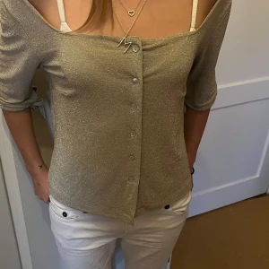 Glittrig guld topp med knappar - Säljer en glittrig guld topp med knappar framtill. Toppen har trekvartsärmar och är perfekt för festliga tillfällen! ✨
