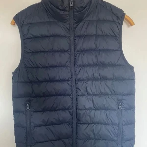 Svart dunväst med dragkedja - Säljer en snygg svart dunväst i mycket bra skick. Västen har en dragkedja framtill och två praktiska fickor med dragkedjor. Perfekt för höst och vår när du vill hålla dig varm utan att bära en jacka. Passar både till vardags och lite mer uppklädda tillfällen.