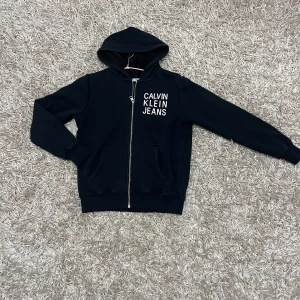  Calvin Klein Jeans Hoodie - Säljer en snygg svart hoodie från Calvin Klein Jeans. Den har en dragkedja framtill och en mysig huva. Perfekt för kyliga dagar och har en stilren design med loggan på bröstet. Passar både till vardags och chillkvällar. 🖤