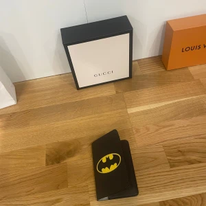 Svart Batman-plånbok - Säljer en cool svart plånbok med Batman-logga i gult. Perfekt för alla Batman-fans! Plånboken är i mycket bra skick och har plats för kort och sedlar. Den är stilren och passar både till vardags och fest. Perfekt presentidé! 🦇